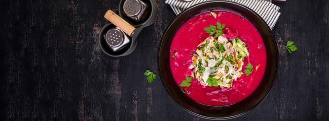 Cold borscht, summer beet soup with fresh cucumber,  boiled egg and boiled chicken fillet on dark table. Traditional European food, delicious lunch. Top view, banner