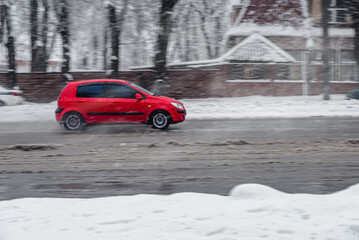 Car riding on city street after blizzard on winter day, navigating a snow-laden urban road, braving the elements of a vigorous snowstorm.