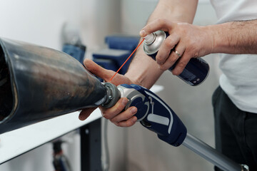 Closeup shot of crop anonymous master spraying penetrating oil on modular knee joint in prosthetics manufacturing factory