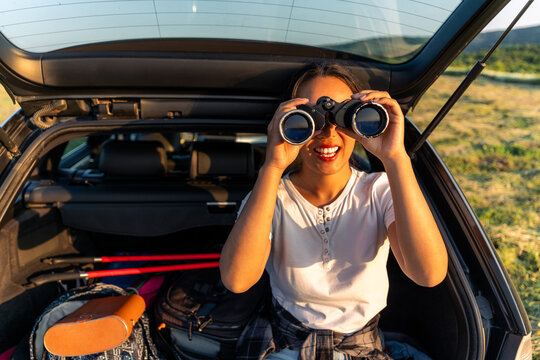 a young woman is sitting in the trunk of her car and using binoculars