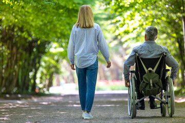 Man in wheelchair walking at park with his wife.