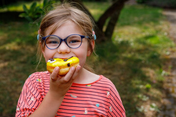 Happy little preschool girl eating sweet donut on summer day. Blond child with doughnut. Cute kid...