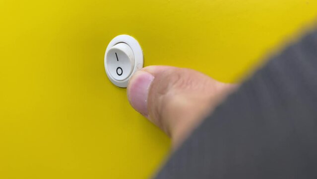 Male right hand thumb turn off switch toggle yellow wall.