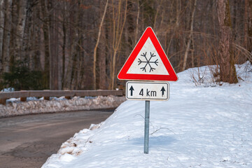 Beware of Ice or snow triangular warning sign by the road in winter