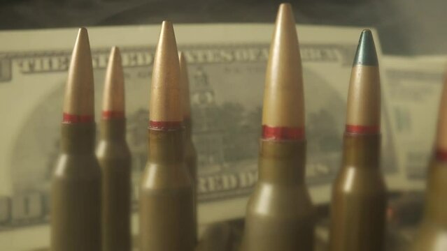 Rows of rifle cartridges on the background of dollar bills close up. Rifle ammunition is shrouded in clouds of smoke. The concept of the sale of weapons under lendlease, help with weapons.
