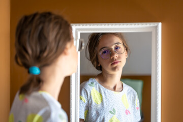 A teenage girl looks at herself in the mirror in the morning.