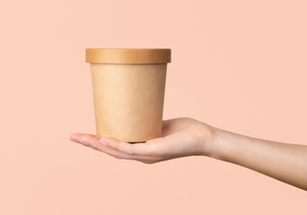 Hand holds craft paper soup cup on isolated pastel background.
