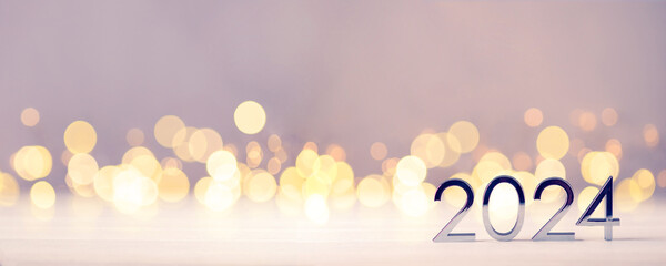 Metal numbers 2024 on a white table with Christmas trees and bokeh lights. Happy New Year 2024 is coming concept. - obrazy, fototapety, plakaty