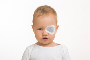White sticking plaster on baby boy eye. Isolated on light gray background. Front view. Closeup....
