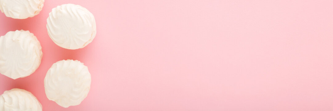 Soft white vanilla zephyr on light pink table background. Pastel color. Closeup. Sweet snack. Food wide banner. Empty place for text. Top down view.