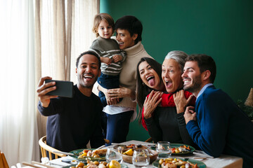 Happy multiracial family taking selfie over smart phone at home on Christmas
