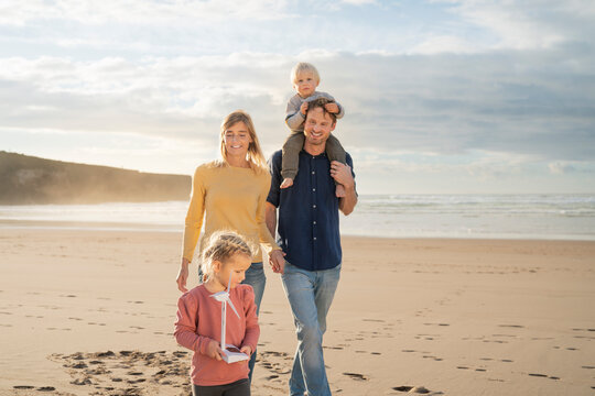 Smiling father and mother walking with children at beach on sunny day