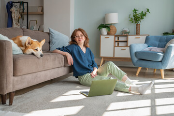 Young woman looking at Welsh Corgi dog on sofa in living room