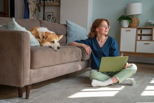 Young freelancer with laptop sitting by pet dog in living room