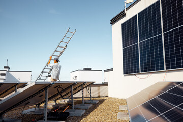 Man carries ladder during solar panels installation on a rooftop of a private house on a sunny day....