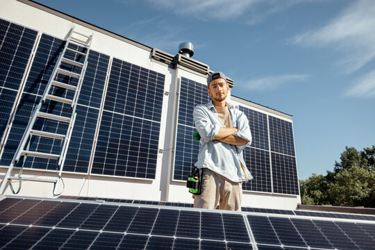 Portrait of handyman standing on a rooftop with installed solar panels on it. Renewable energy for self consumption concept