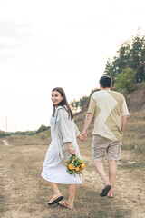 A man and a woman with flowers are walking in a meadow, a happy couple.