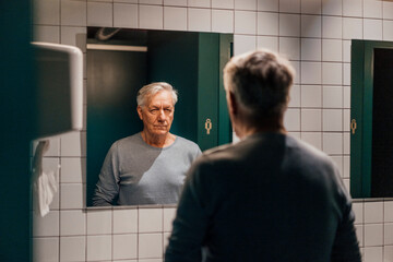 Senior man looking in mirror in bathroom
