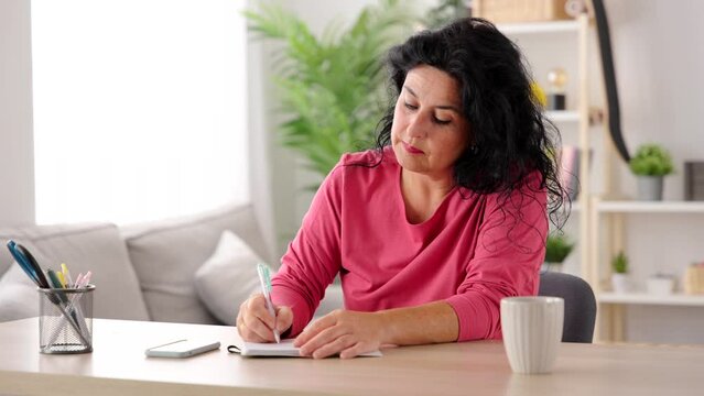 Middle aged woman writing diary on notebook.