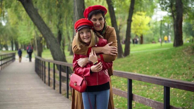 Medium shot portrait of Caucasian grandmother hugging granddaughter looking at camera smiling. Happy senior woman posing with teenage girl in autumn park on alley