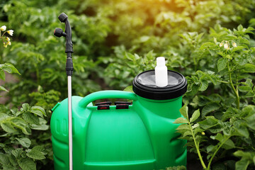 White little bottle of pesticide, herbicide for protecting plants from diseases and pests with mock up stands on container sprayer on natural green garden background. Agricultural seasonal work
