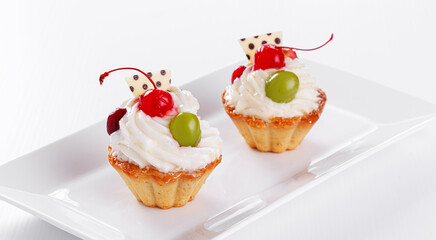 Beautiful cream cakes with cherries and grapes on a plate on a white background