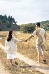 A man and a woman walk into a field holding hands.