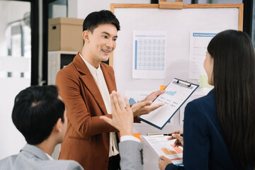 Asian businessman showing hand and smiling young team of colleagues making good business discussion in modern coworking office concept teamwork people.