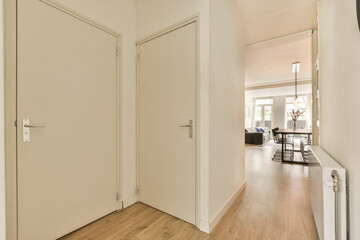 a hallway with white walls and wood flooring on the right side, there is an open door leading to another room