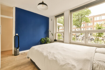 a bedroom with blue walls and white bedding in front of a large window that looks out onto the street