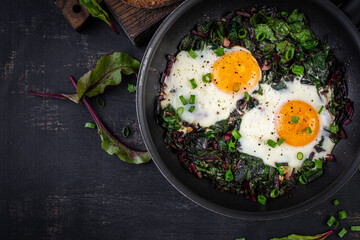 Breakfast. Fried eggs with green beet leaves, garlic, pepper and green onion in pan. Top view, flat lay