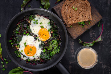 Breakfast. Fried eggs with green beet leaves, garlic, pepper and green onion in pan. Top view, flat lay