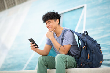 young smiling man sitting with mobile phone and bag