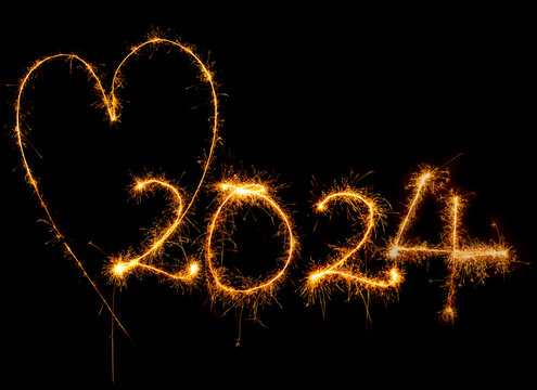 Herz und Jahreszahl 2024 mit Wunderkerze geschrieben vor dunklem Hintergrund.