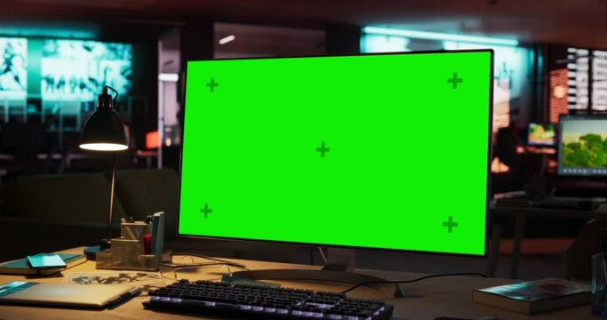 Computer Monitor with Green Screen Standing on a Wooden Desk with Height Adjustable Function. Chroma Key Display in Empty Decorated Creative Office for Game Development Startup. Zoom In Shot