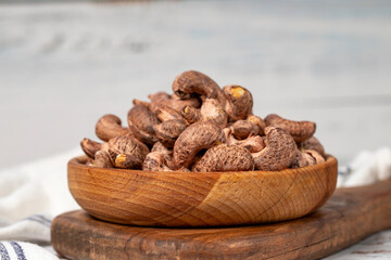 Cashews with shell in wood bowl. Shelled cashew on white wood background