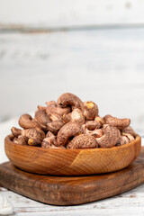 Cashews with shell in wood bowl. Shelled cashew on white wood background. Close up