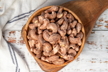 Cashews with shell in wood bowl. Shelled cashew on white wood background. Top view