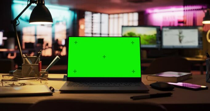 Zoom in Shot of Laptop Computer Standing on a Wooden Desk with a Green Screen Chromakey Mock Up Display. Creative Office Working Station for Game Developer and Graphic Designer in Creative Agency
