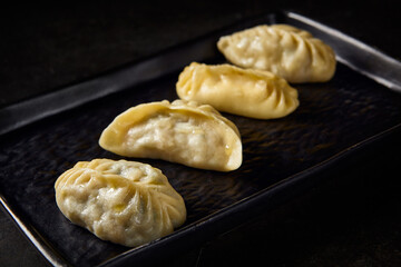 Close-up of Uzbek manty, highlighting its texture and filling, served on a black plate set on a black marble table