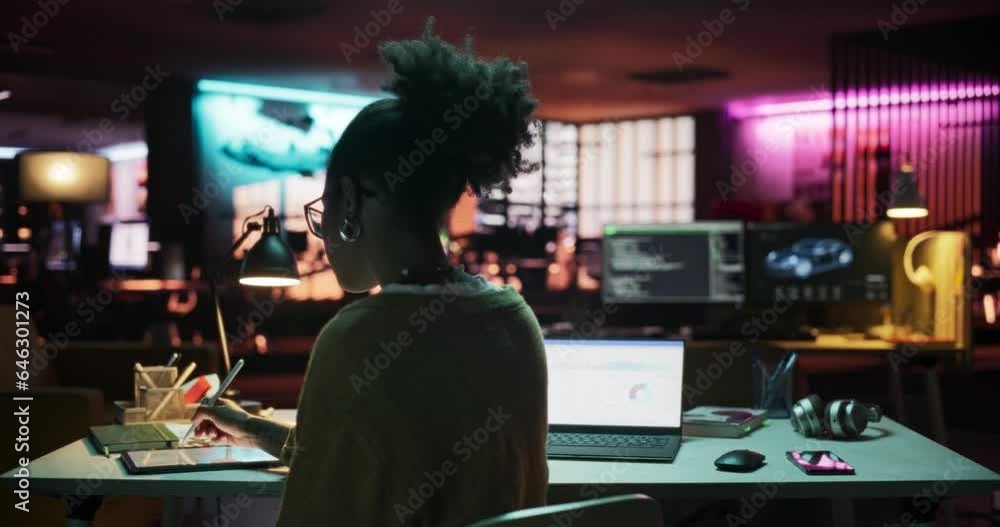 Poster backview: motivated black female using laptop and tablet computer in creative agency in the evening,