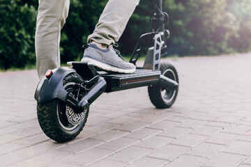 A man's foot stands on the platform of a scooter. Close-up of a man riding a black electric...