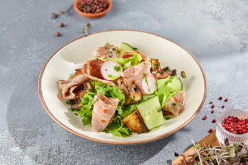 High-angle view of a vibrant salad with baked meat, vegetables, and sauce. Set on a ceramic plate against a minimalist gray concrete background