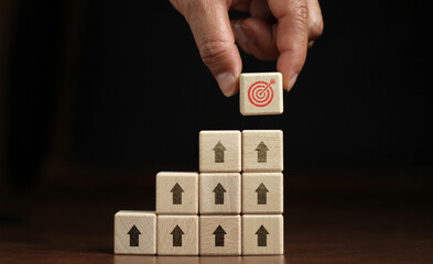 Arrow on wooden block pointing at target icon on wooden block with businessman's hand placing red dartboard symbol. Business Agenda and Mission Concepts Cube dartboard. Future vision strategy, goal, s