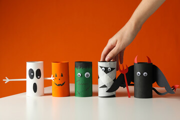 Handmade paper halloween characters on white table and hand on orange background