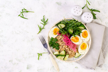 Breakfast oatmeal porridge with boiled eggs, cucumber, red onion and greens. Healthy balanced food. Top view