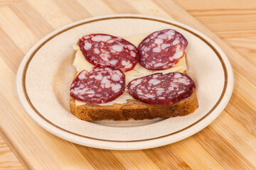 Open sandwich with dry-cured sausage and cheese on saucer