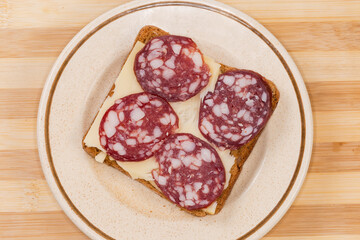 Open sandwich with dry-cured sausage and cheese on saucer