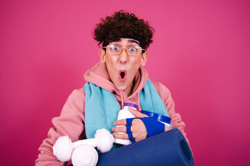 Young attractive curly man posing on a pink background and doing fitness.