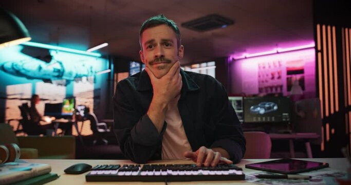 Portrait of a Male Software Developer Writing Code in a Creative Office with Neon Lights. Young Man Focused on Typing on Keyboard and Working on Desktop Computer. Point of View of Screen Monitor
